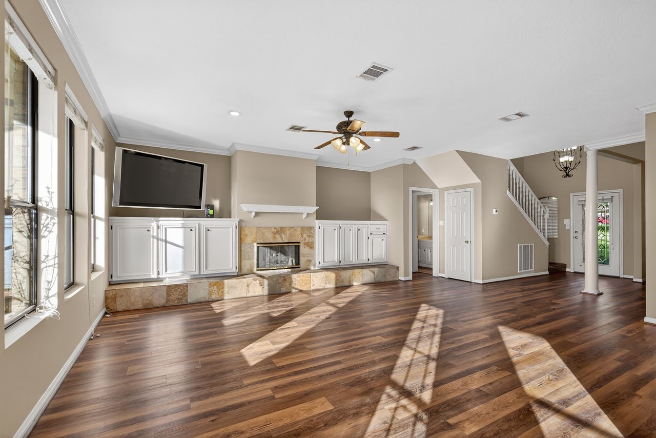 12626 Aries Loop Willis, TX 77318 - Photo 8 of 50 Spacious living room with wood flooring, large windows, and abundant natural light. Features a fireplace with built-in cabinetry, ceiling fan, and neutral color palette. Open layout with stairway and access to a side room, perfect for entertaining or relaxing.