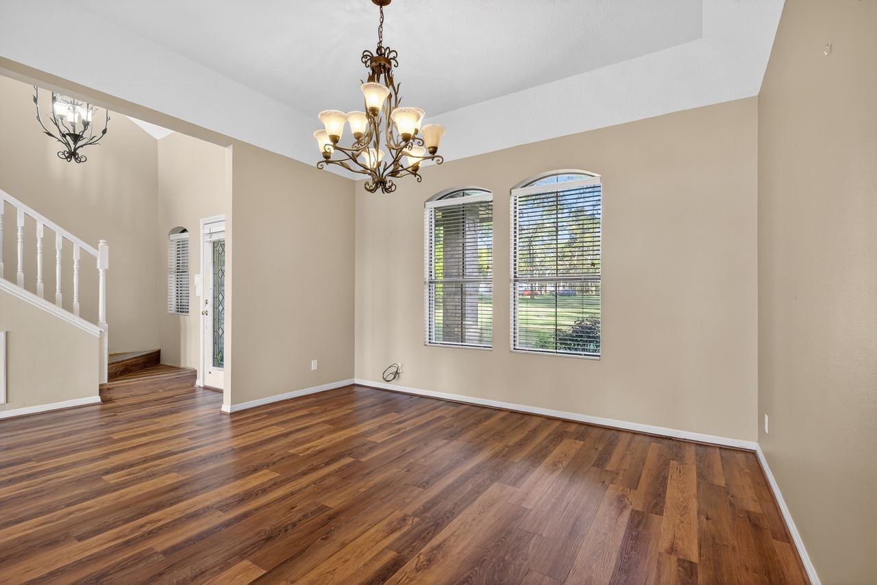 12626 Aries Loop Willis, TX 77318 - Photo 9 of 50 This photo showcases a bright, open living space with large windows, hardwood floors, and a stylish chandelier. The adjacent staircase leads to the upper level, adding to the home's elegant charm.