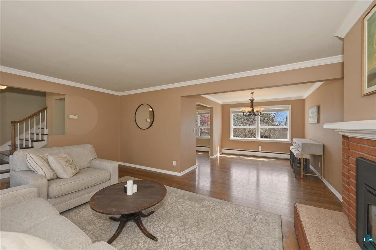 1918 West Kent Road Duluth, MN 55812 - Photo 12 of 42 Spacious living area featuring wood-finish flooring, a brick fireplace with a white mantel, and crown molding