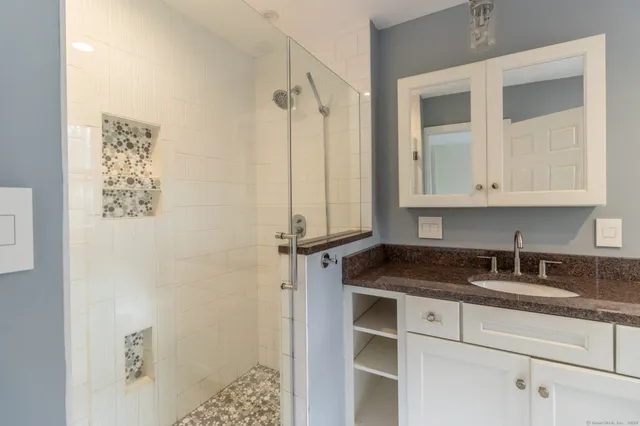 a bathroom with a granite countertop sink a mirror and shower