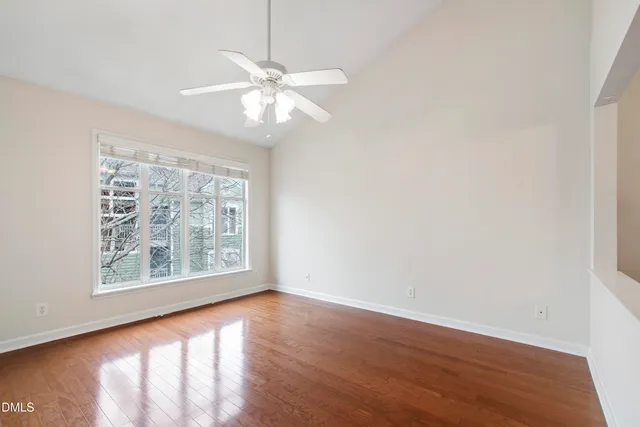 an empty room with wooden floor chandelier fan and windows