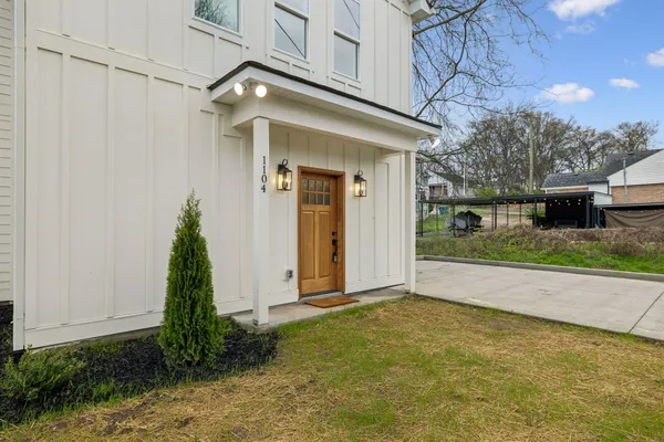 a view of a white house with a large windows and a yard with plants and large trees