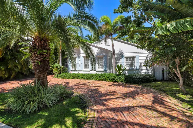 a view of a white house with a big yard plants and palm trees