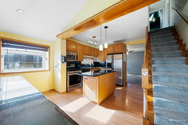 a kitchen with stainless steel appliances kitchen island granite countertop a refrigerator a stove and a wooden cabinets