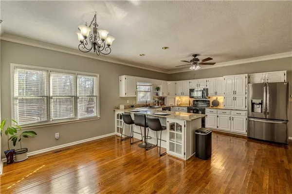 a kitchen with stainless steel appliances granite countertop a stove top oven a refrigerator a dining table and chairs with wooden floor