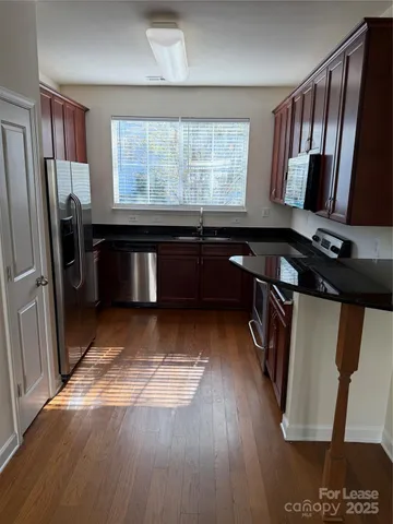 a kitchen with stainless steel appliances granite countertop a refrigerator a sink dishwasher a stove a dining table and wooden floor