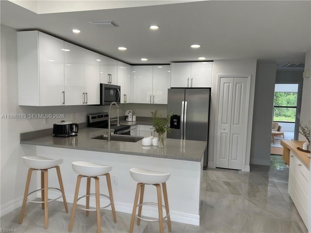 4854 30th Street Southwest, Unit 4854 Lehigh Acres, FL 33973 - Photo 2 of 11 a kitchen with stainless steel appliances granite countertop a refrigerator a stove a sink a dining table and chairs