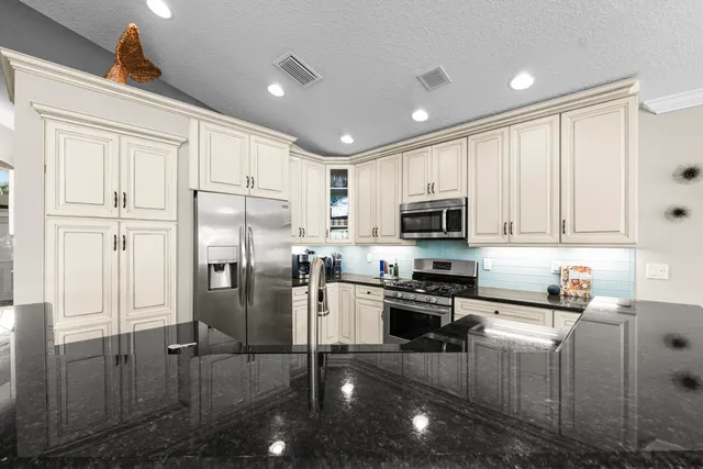 a kitchen with stainless steel appliances granite countertop a refrigerator a sink a stove and white cabinets