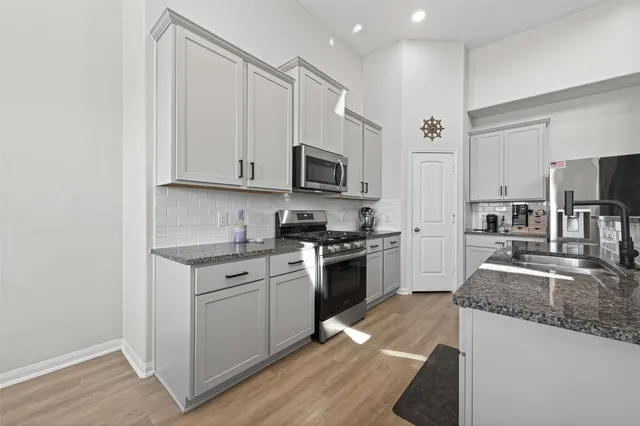 a kitchen with granite countertop a sink a stove top oven a refrigerator cabinets and wooden floor