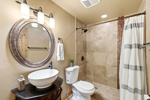 5404 Mountain View Road Coalville, UT 84017 - Photo 37 of 50 Vessel sink with dark countertop, ornate vanity, round framed mirror, three-light vanity fixture, and tiled shower with accent band