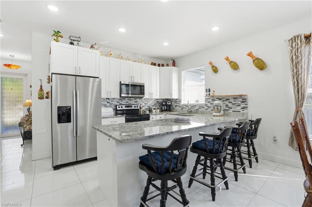 3409 64th Street West Lehigh Acres, FL 33971 - Photo 16 of 44 a kitchen with stainless steel appliances a refrigerator a stove a sink and white cabinets with wooden floor