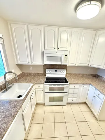 a kitchen with granite countertop a sink a stove top oven and cabinetry
