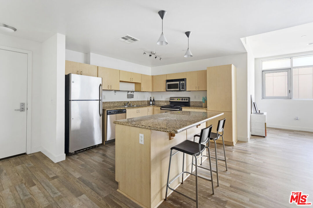 a kitchen with stainless steel appliances granite countertop a refrigerator a stove top oven a sink dishwasher a dining table and chairs with wooden floor