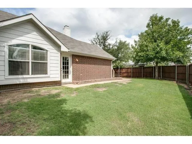 a backyard of a house with plants and large tree