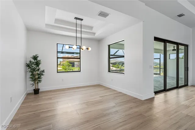 an empty room with wooden floor chandelier and windows
