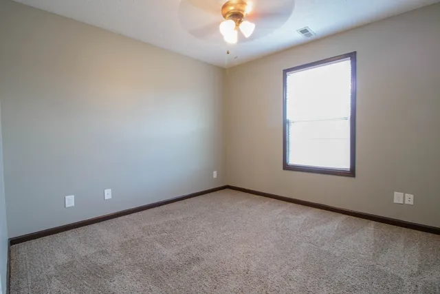 an empty room with a chandelier fan and windows