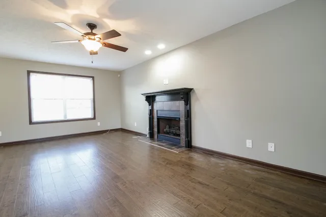 an empty room with wooden floor chandelier fan and windows