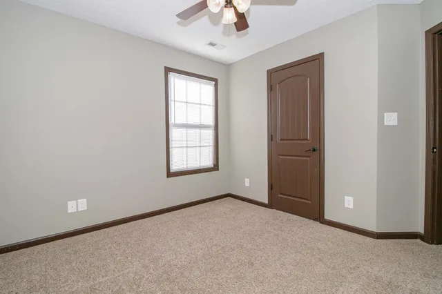 an empty room with chandelier fan and windows