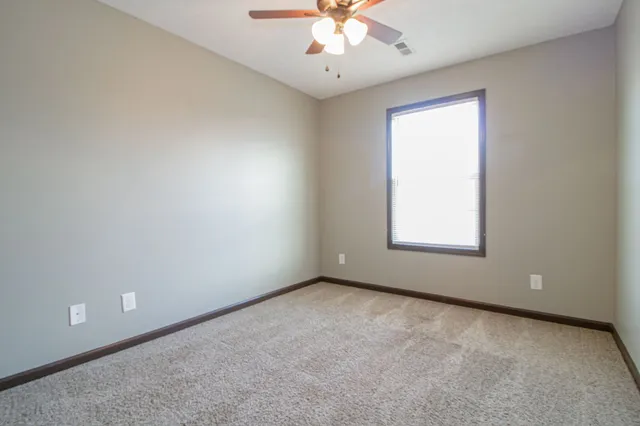 an empty room with a chandelier fan and windows