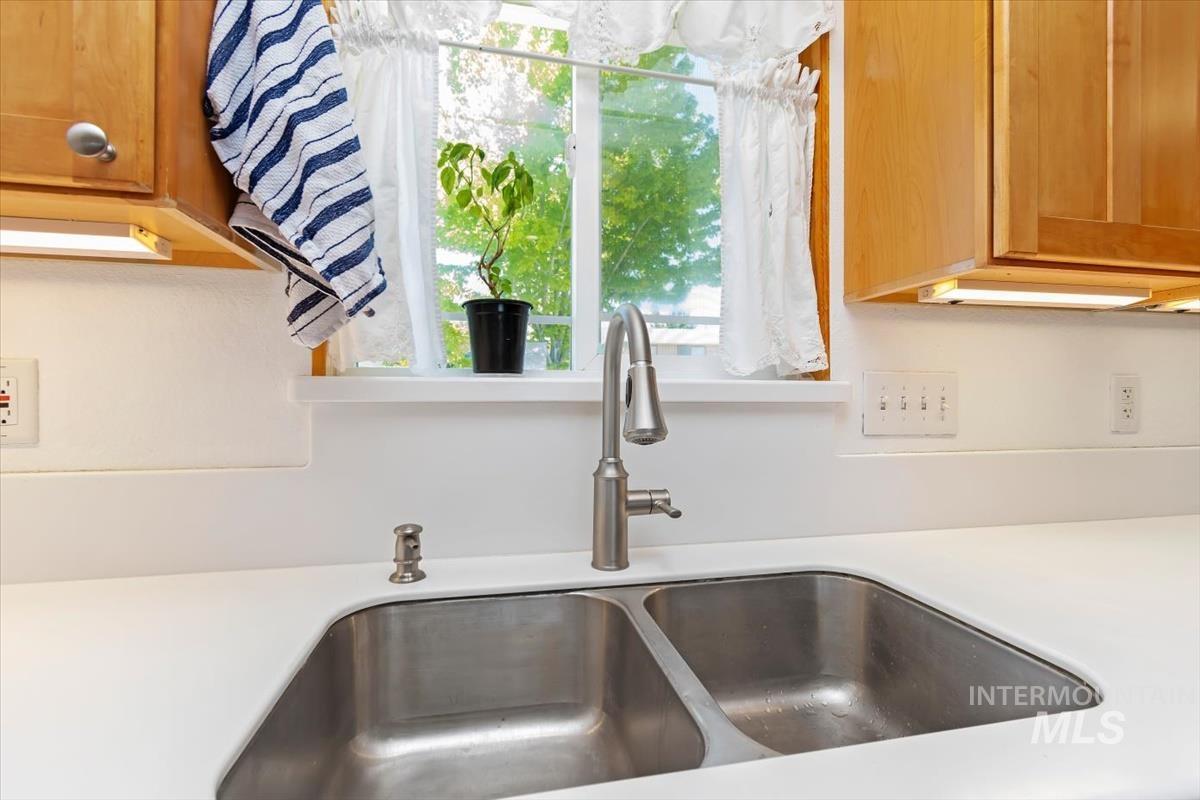 10178 West Fox Ridge Drive Boise, ID 83709 - Photo 12 of 36 Kitchen sink area featuring a dual-basin stainless steel sink with a high-arc faucet, solid surface countertop, and wood-finish cabinetry with under-cabinet lighting