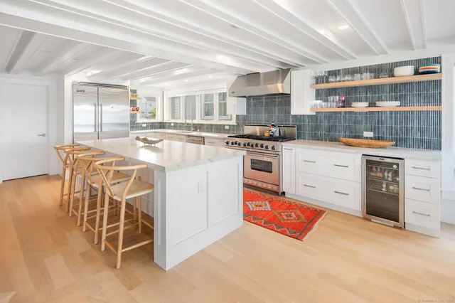 a kitchen with stainless steel appliances kitchen island granite countertop a stove top oven a sink dishwasher and white cabinets with wooden floor
