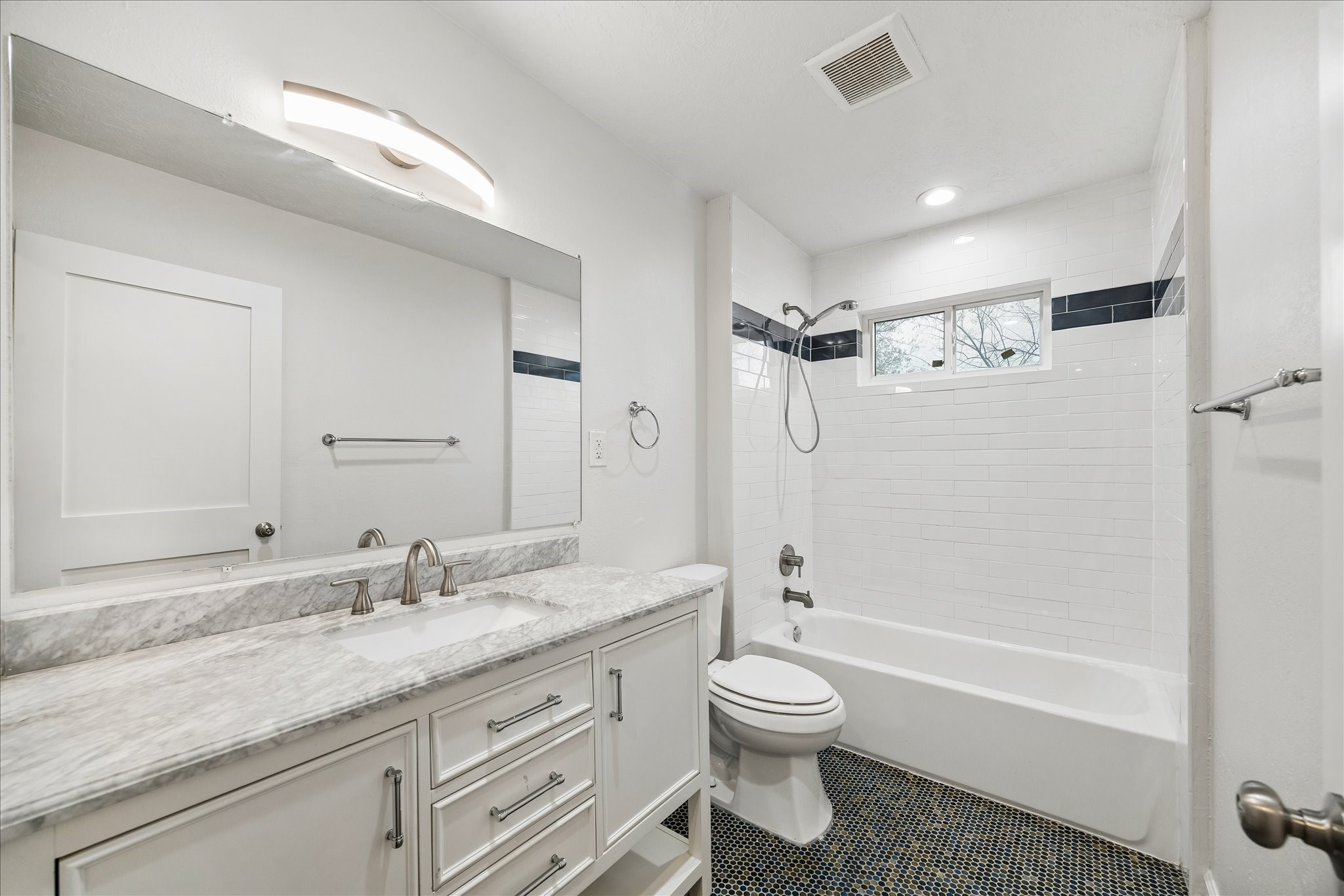7515 Magnolia Street Houston, TX 77023 - Photo 13 of 16 This bright, fully updated secondary bath features a marble dual-sink vanity, sleek modern fixtures, and a large framed mirror. The shower/tub combo is finished with crisp white subway tile accented by a bold decorative band and complemented by a window that brings in natural light. Mosaic tile flooring adds texture and visual interest, creating a clean, timeless, and move-in-ready space. A nearby hall linen closet provides additional storage and complements this generously sized bath.