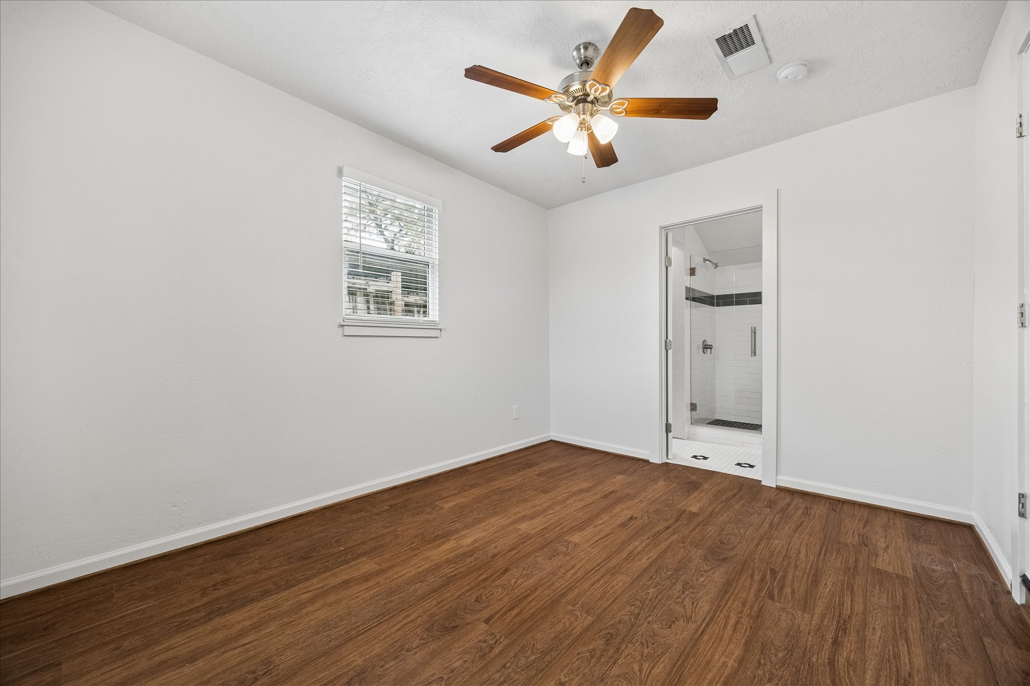 7515 Magnolia Street Houston, TX 77023 - Photo 8 of 16 The 10×12 primary bedroom is situated in its own private wing and features beautiful hardwood flooring, a ceiling fan with light, a large walk-in closet, and an ensuite primary bath. This well-designed layout offers comfort, privacy, and convenience.