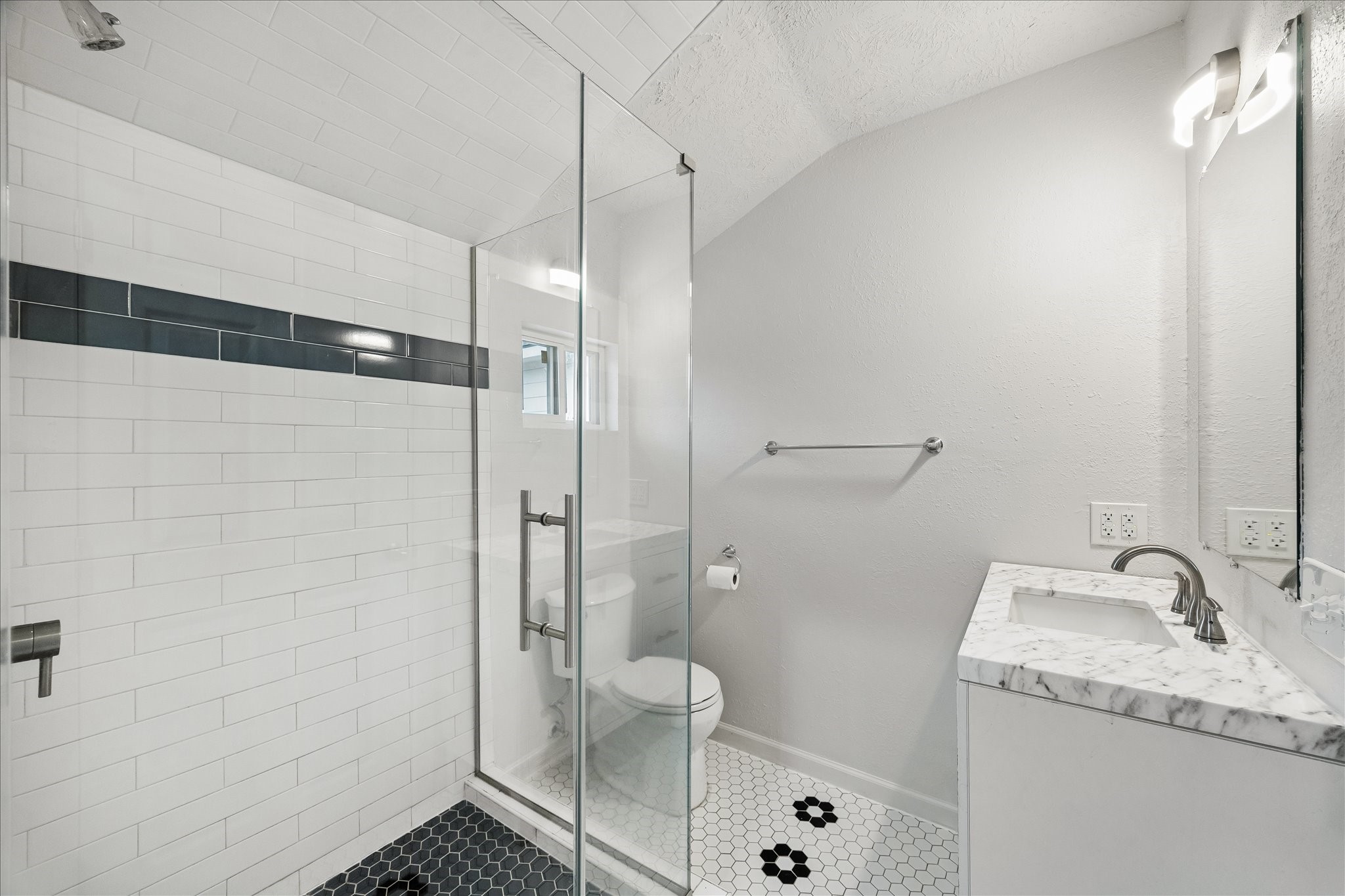 7515 Magnolia Street Houston, TX 77023 - Photo 9 of 16 Stylish primary bath showcasing a glass-enclosed walk-in shower with classic white subway tile and a bold accent band. Marble vanity top, modern fixtures, and timeless black-and-white tile flooring create a clean, sophisticated look with a touch of character.