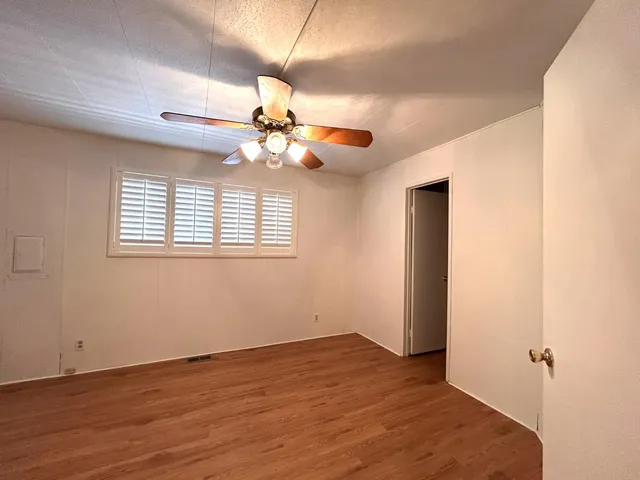 an empty room with wooden floor chandelier fan and windows