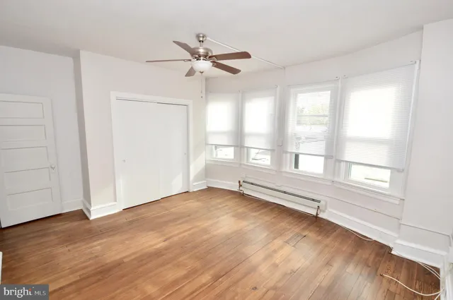 an empty room with wooden floor fan and windows