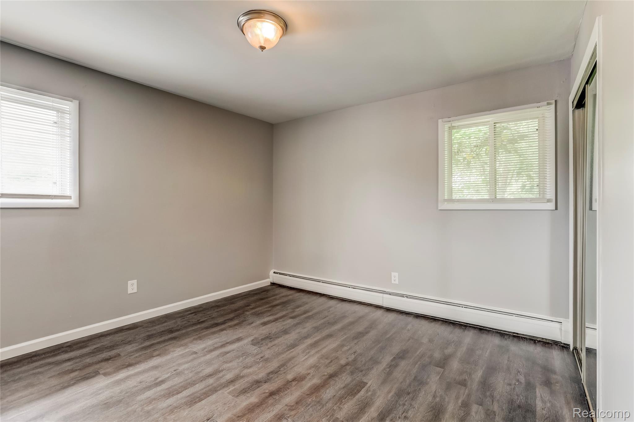 649 West Maple Road, Unit 8 Clawson, MI 48017 - Photo 10 of 16 Neutral wall paint, wood-finish flooring, two windows with blinds, and a built-in closet with mirrored sliding doors