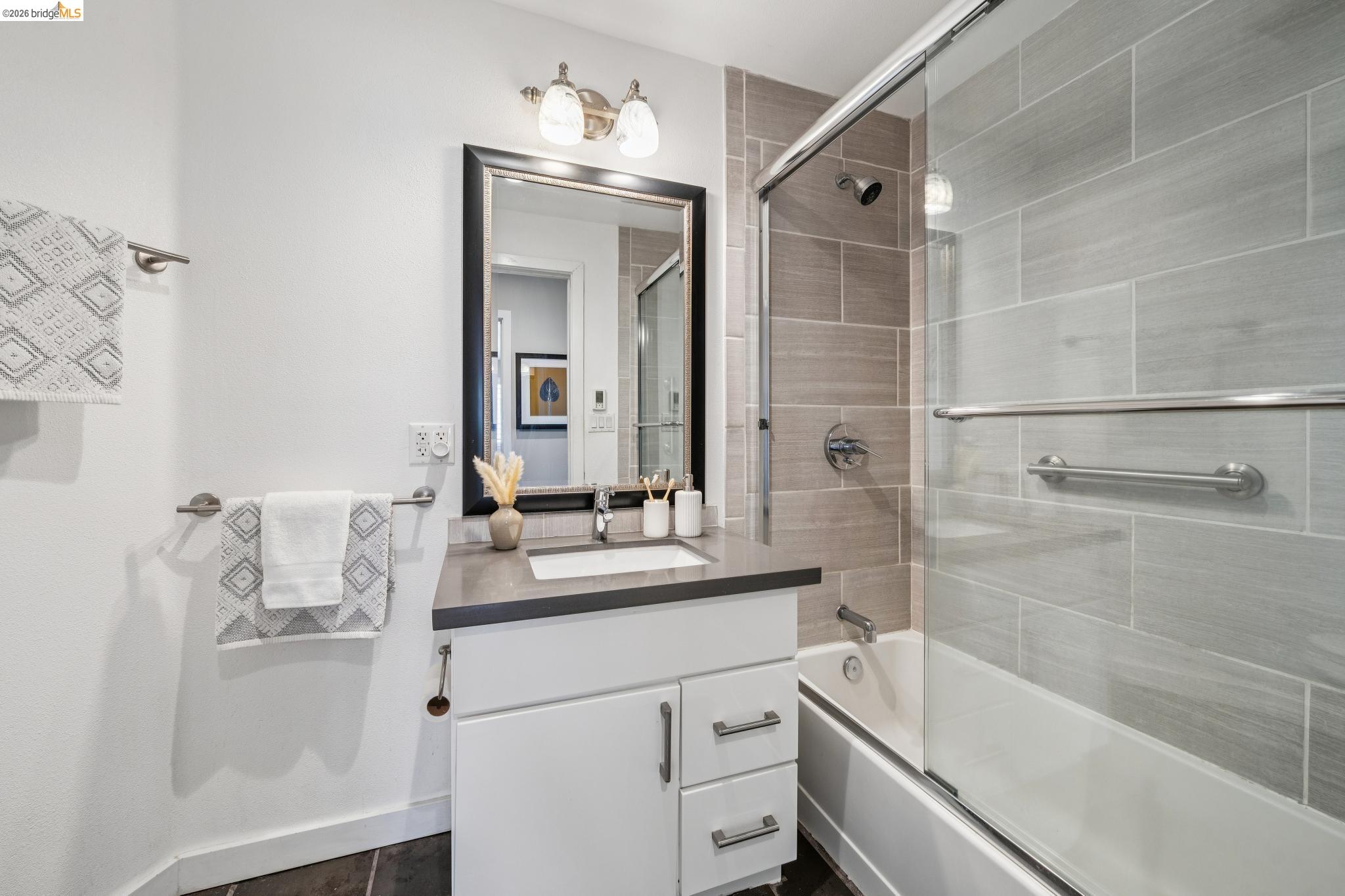 1394 Queens Road Berkeley, CA 94708 - Photo 50 of 63 White vanity with a single sink and dark countertop, framed mirror, and a wall-mounted light fixture