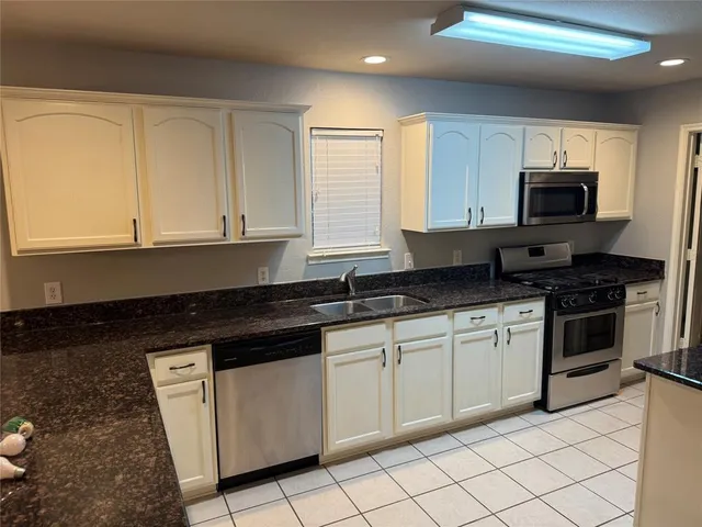 a kitchen with granite countertop white cabinets sink and stainless steel appliances