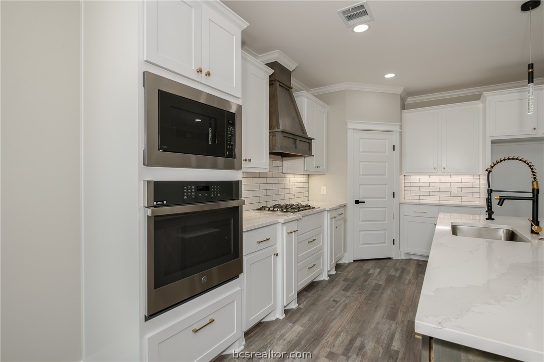 2908 GOLDBERG Drive Bryan, TX 77808 - Photo 21 of 44 Modern kitchen features: stainless steel appliances, quartz countertops, stained island, painted cabinets, decorative pendant lights, cabinet hardware, vinyl flooring, and tile backsplash.