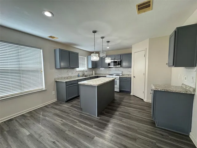 a large kitchen with stainless steel appliances granite countertop a stove top oven a sink dishwasher and a refrigerator with wooden floor