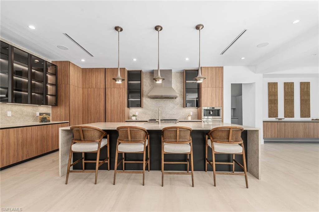 1800 Crayton Road Naples, FL 34102 - Photo 7 of 32 Kitchen with light stone counters, glass insert cabinets, a large island, a kitchen breakfast bar, and recessed lighting