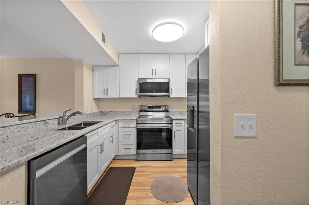 8264 Key Royal Circle, Unit 812 Naples, FL 34119 - Photo 5 of 21 Kitchen featuring a textured wall, stainless steel appliances, light stone counters, white cabinetry, and light wood finished floors