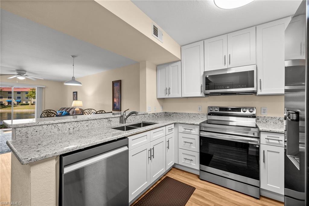 8264 Key Royal Circle, Unit 812 Naples, FL 34119 - Photo 6 of 21 Kitchen featuring stainless steel appliances, light stone countertops, a peninsula, a ceiling fan, and light wood-style flooring