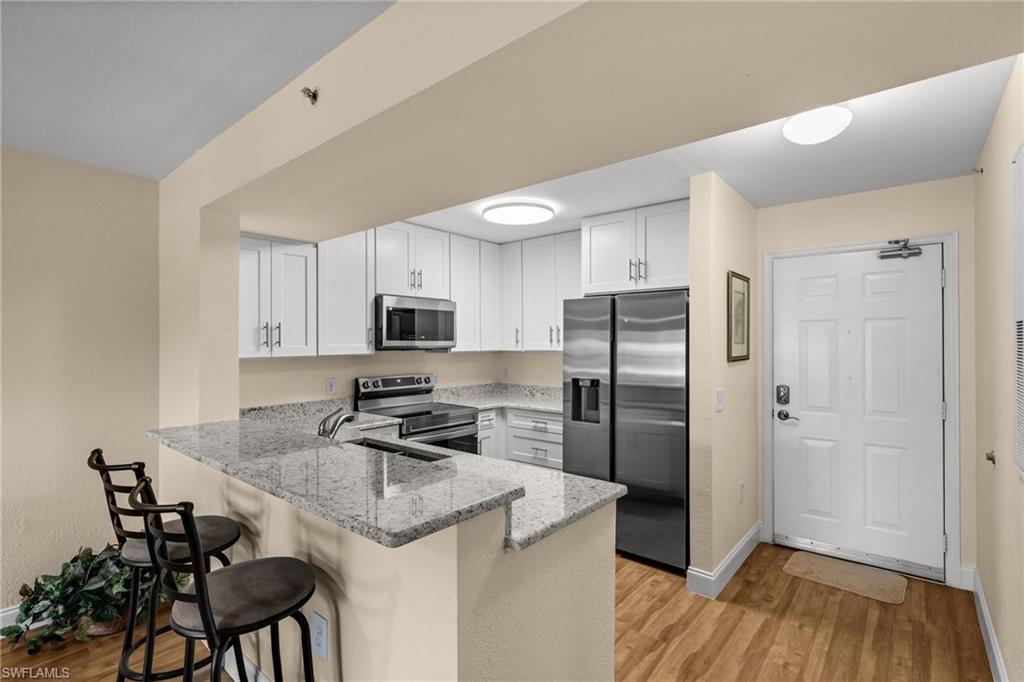 8264 Key Royal Circle, Unit 812 Naples, FL 34119 - Photo 7 of 21 Kitchen featuring light stone counters, a peninsula, stainless steel appliances, a kitchen breakfast bar, and white cabinets