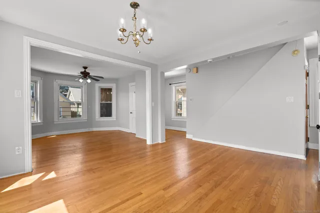 a view of an empty room with chandelier and wooden floor