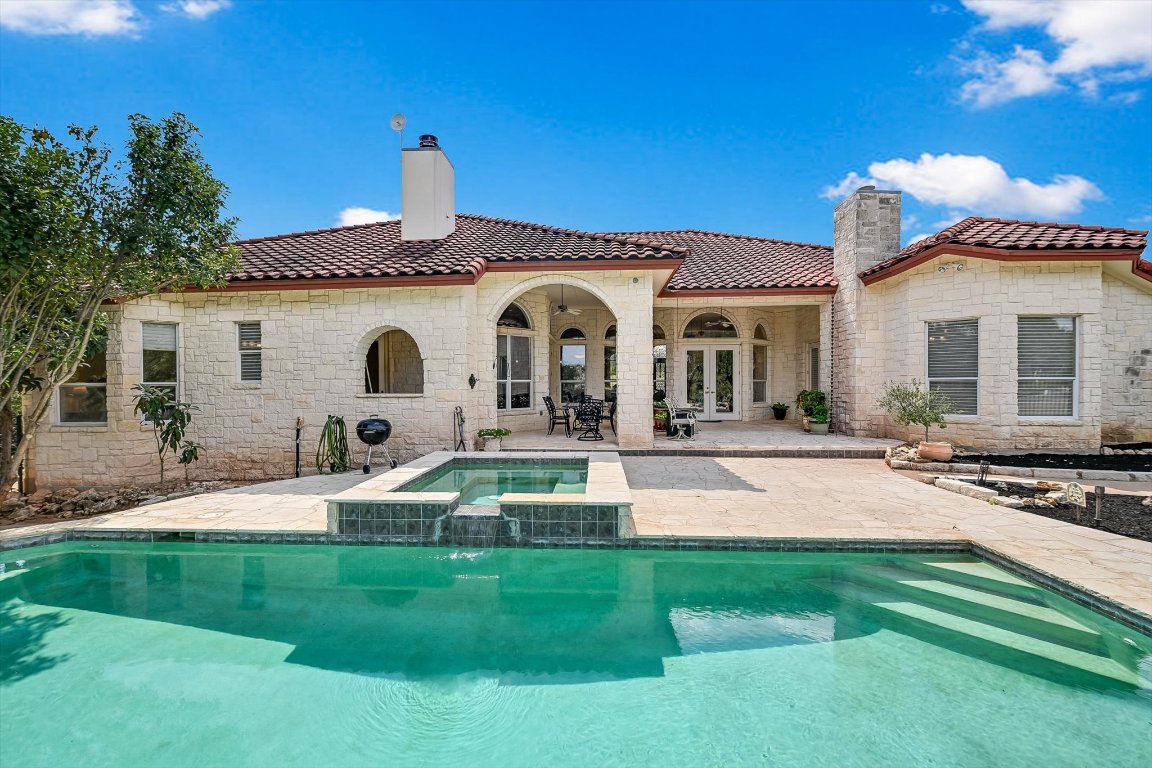 1001 Wesley Ridge Drive Spicewood, TX 78669 - Photo 2 of 35 Rear view of house featuring a patio area, a chimney, a tiled roof, stone siding, and french doors