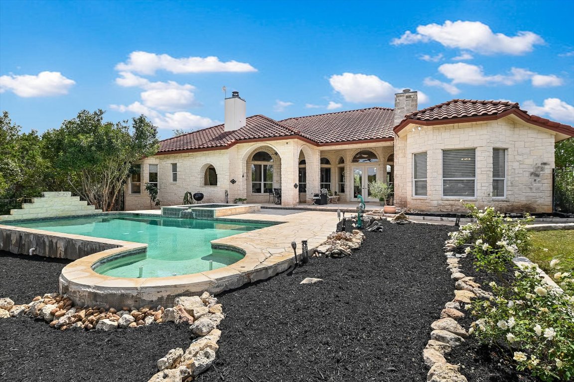 1001 Wesley Ridge Drive Spicewood, TX 78669 - Photo 20 of 35 Back of property with a chimney, a tiled roof, a patio, a pool with connected hot tub, and stone siding
