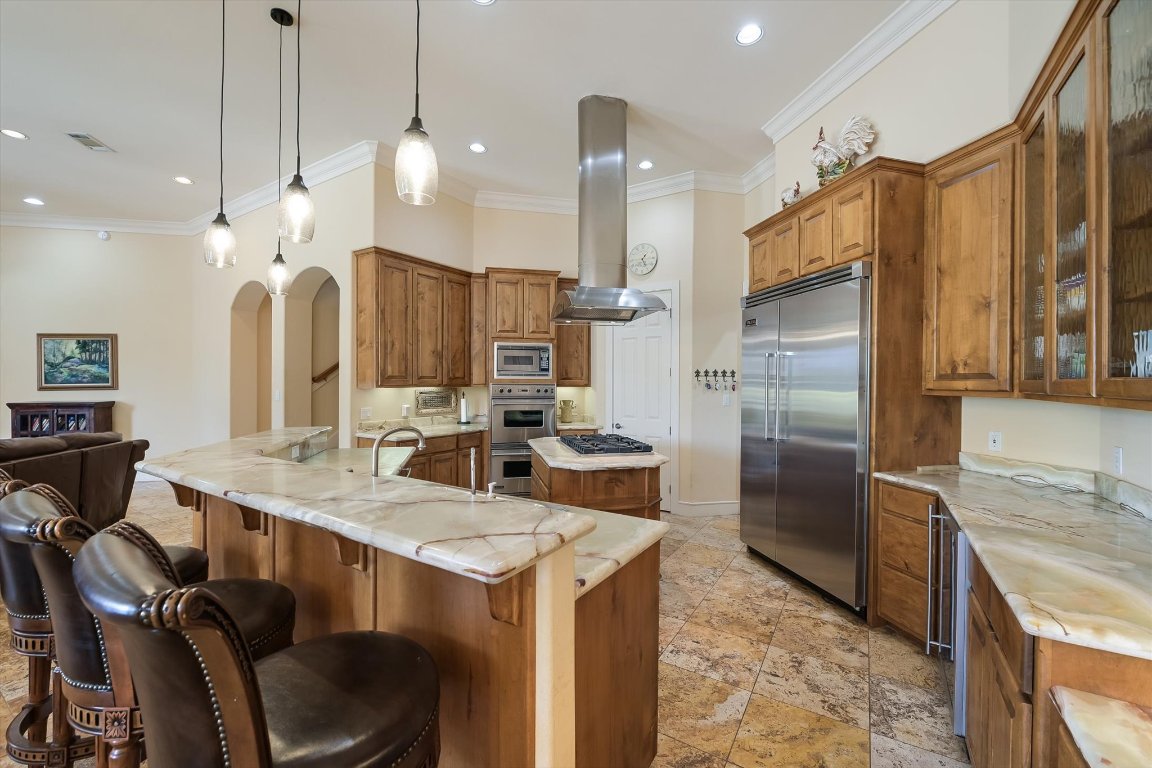 1001 Wesley Ridge Drive Spicewood, TX 78669 - Photo 3 of 35 Kitchen with brown cabinetry, a kitchen island, glass insert cabinets, ornamental molding, and built in appliances