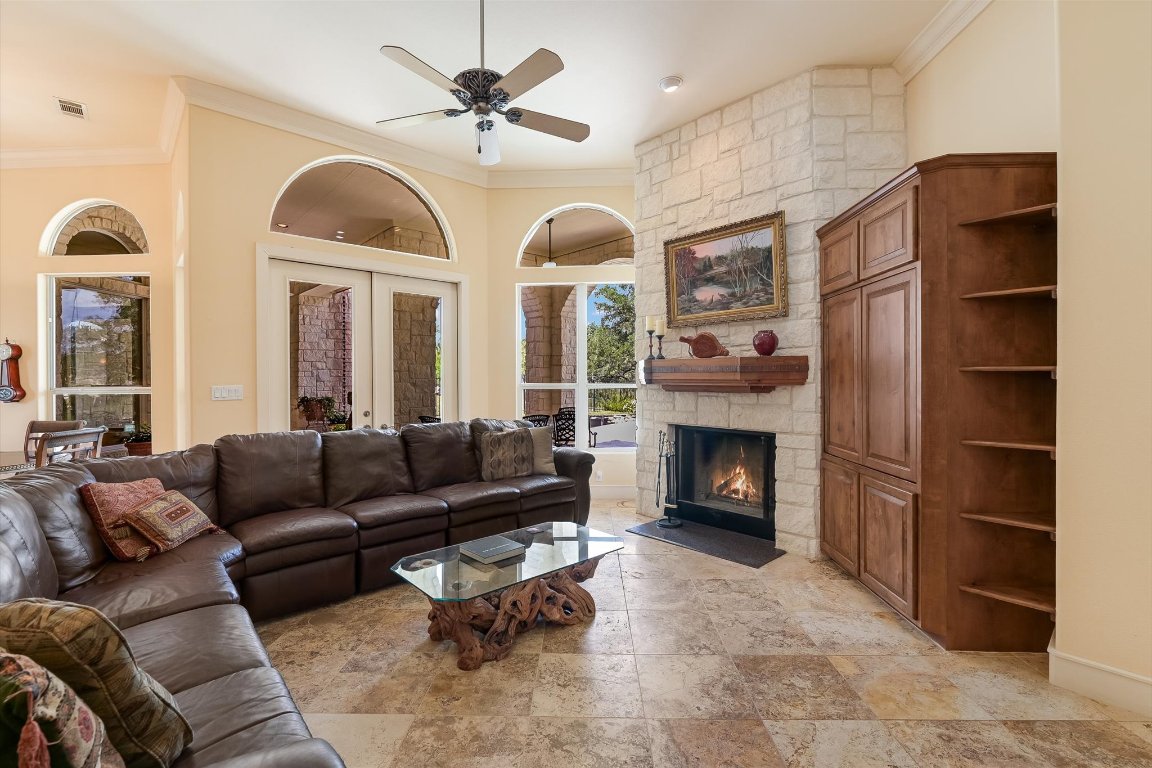 1001 Wesley Ridge Drive Spicewood, TX 78669 - Photo 6 of 35 Living area featuring crown molding, ceiling fan, a stone fireplace, french doors, and stone tile flooring
