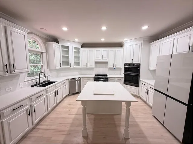 a large kitchen with stainless steel appliances kitchen island granite countertop a refrigerator a sink dishwasher a stove with white cabinets and wooden floor