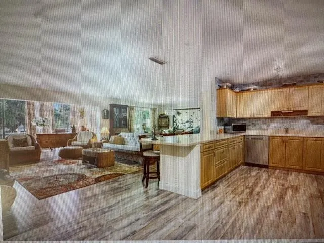 a large white kitchen with granite countertop a stove a sink dishwasher and a dining table with wooden floor