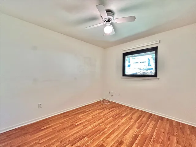 an empty room with wooden floor chandelier fan and windows