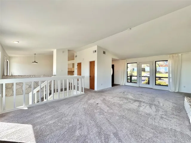 a view of an empty room with windows & stairs