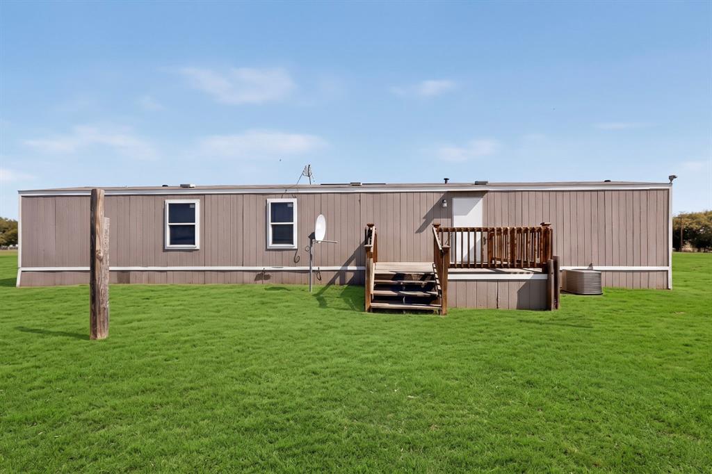 15281 Stice Road Krum, TX 76249 - Photo 22 of 22 Expansive green lawn, wood-finish exterior siding, white frame windows, wood deck with railings, and a white entry door