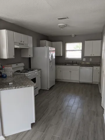 a kitchen with granite countertop a refrigerator a stove a sink dishwasher and white cabinets with wooden floor